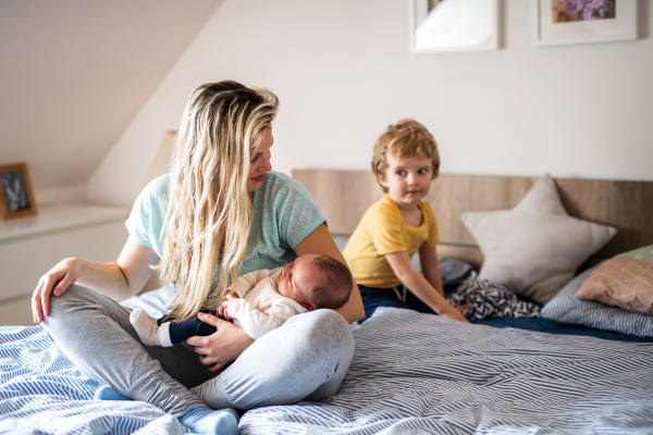 A beautiful young mother with a newborn baby and his toddler brother at home, sitting on bed.