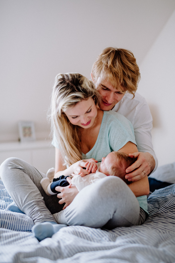 Beautiful young parents holding a newborn baby at home, sitting on bed.