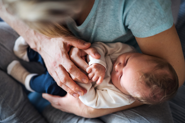 A midsection of young parents with a newborn baby at home, top view.