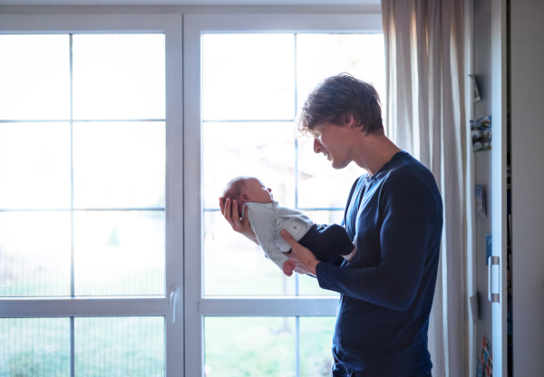 A happy young father holding a newborn baby at home, looking at him. Copy space.