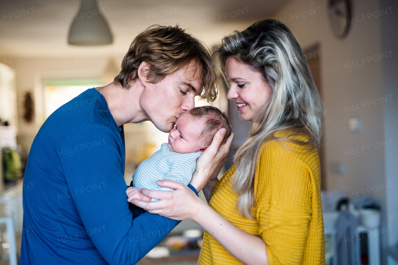 Beautiful young parents holding a newborn baby at home, kissing.