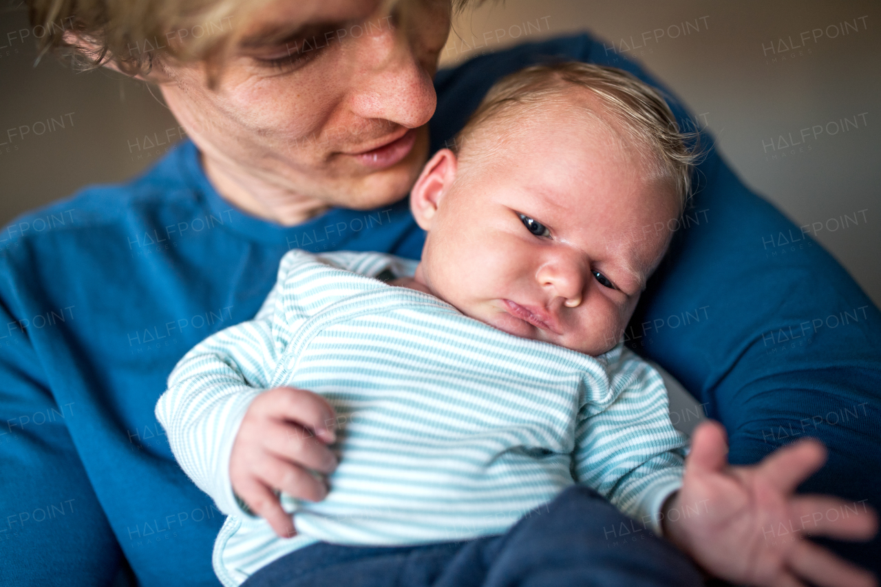 A close -up of young father holding a newborn baby at home, front view.