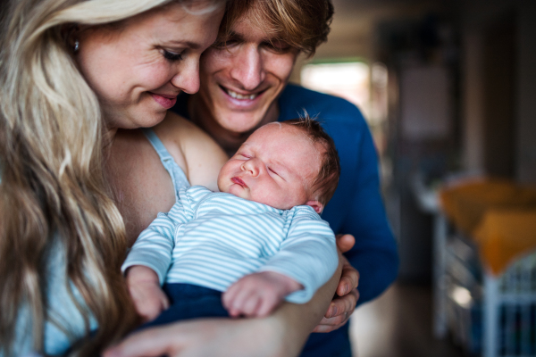 Beautiful young parents holding a newborn baby at home.