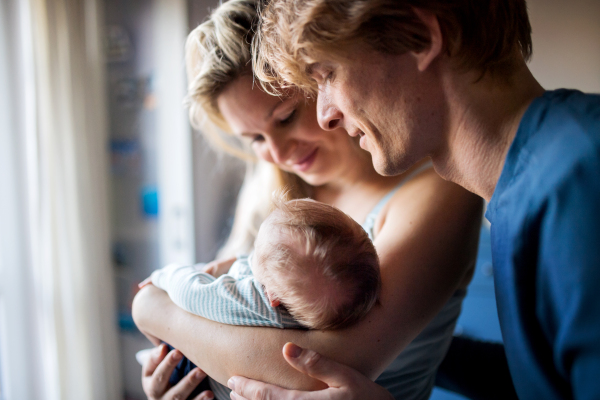 Beautiful young parents holding a newborn baby at home.