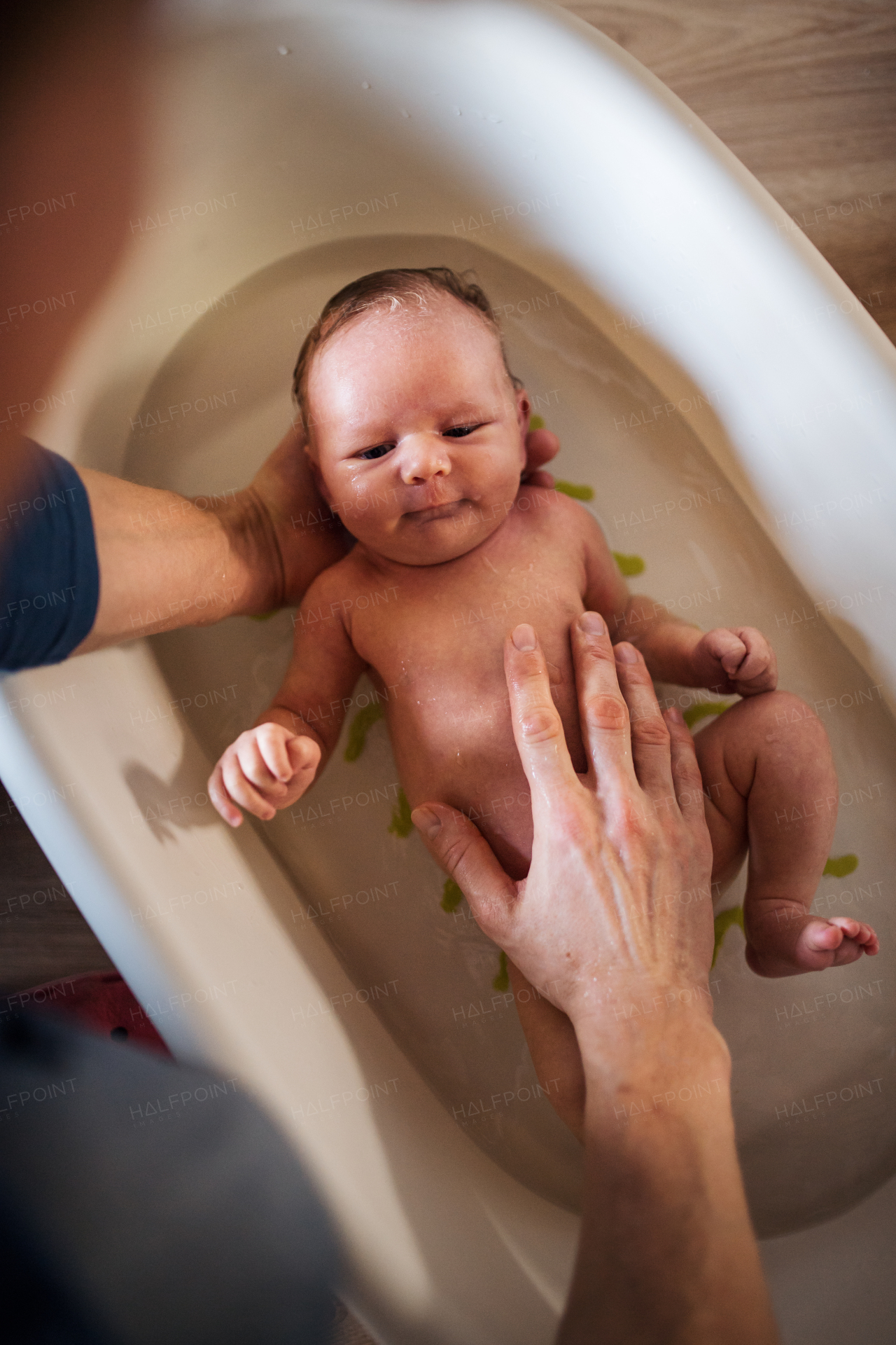 Top view of unrecognizable parent giving a happy newborn baby a bath at home.