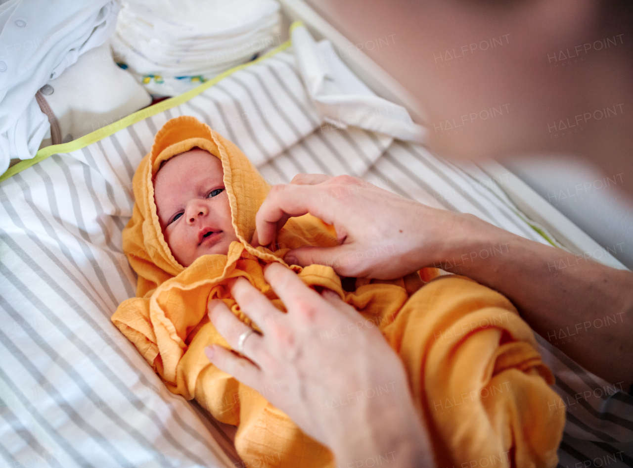 Unrecognizable father drying a newborn baby with a towel after a bath at home.