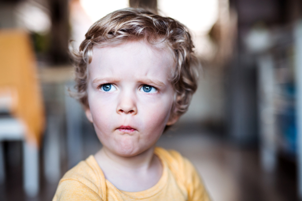 A front view of a sad toddler boy at home.