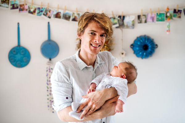 A front view of young father holding a newborn baby at home.