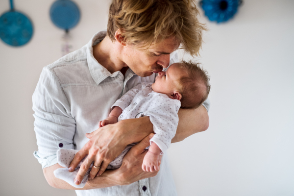 A front view of young father holding a newborn baby at home, kissing him.