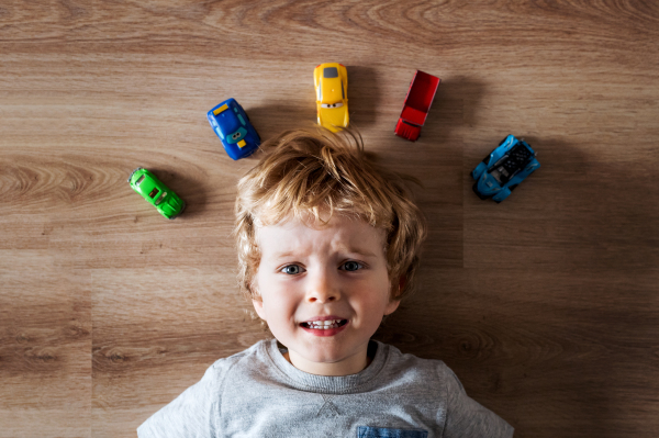 A top view of a toddler boy with toy cars lying on the floor at home.