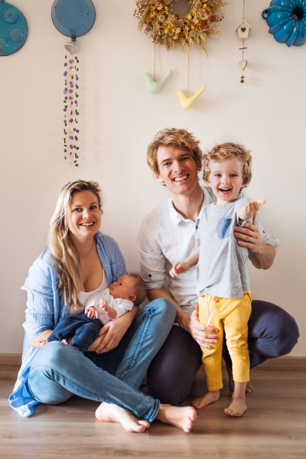 Portrait of young parents with a newborn baby and small toddler son at home.