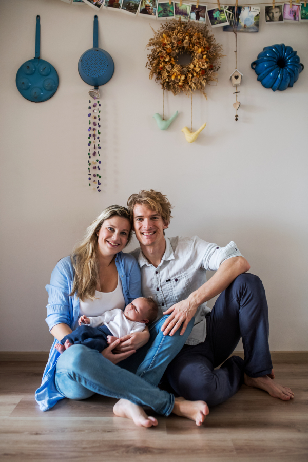 A portrait of beautiful young parents holding a newborn baby at home.