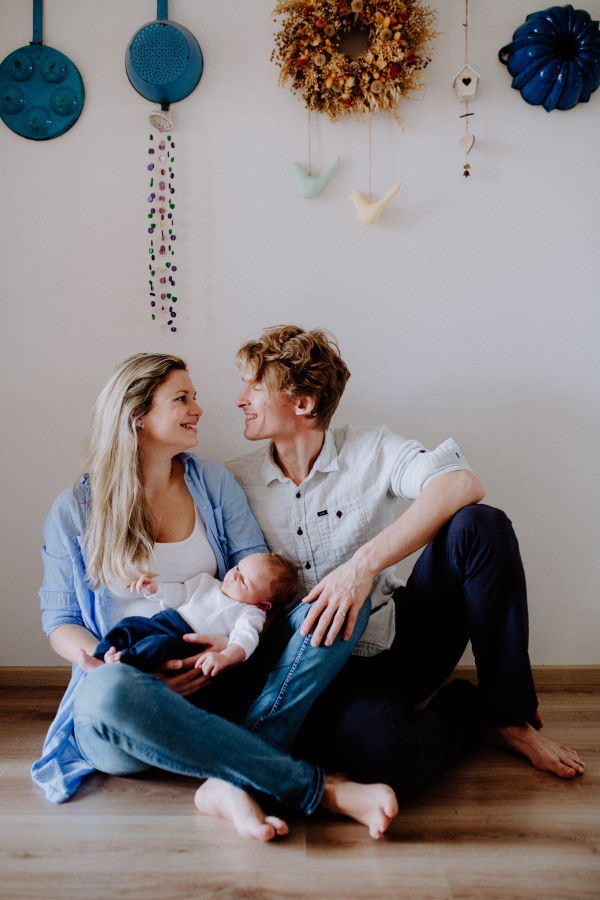 A portrait of beautiful young parents holding a newborn baby at home.