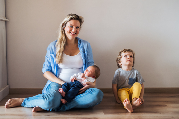 A beautiful young mother with a newborn baby and his toddler brother at home.