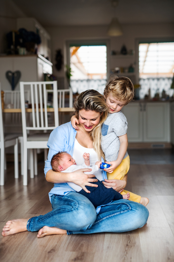 A beautiful young mother with a newborn baby and his toddler brother at home.