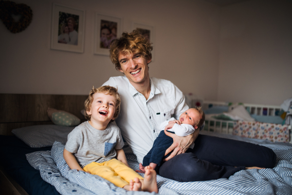 A young father holding a newborn baby and toddler son at home.