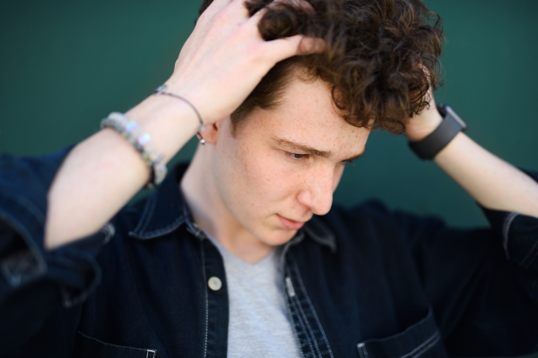 A close-up portrait of young man against green background outdoors, standing.