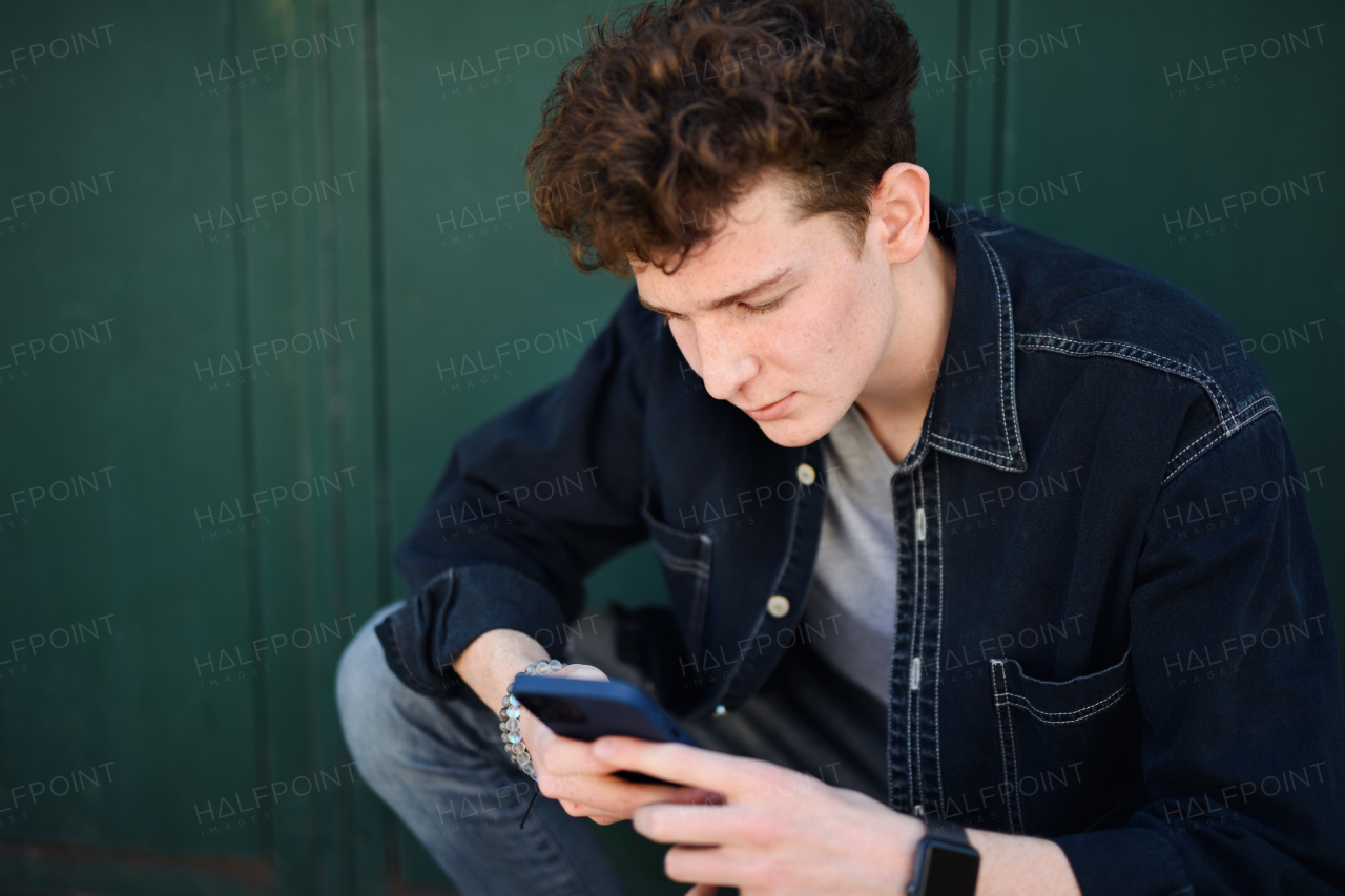 A portrait of young man against green background outdoors, using smartphone.