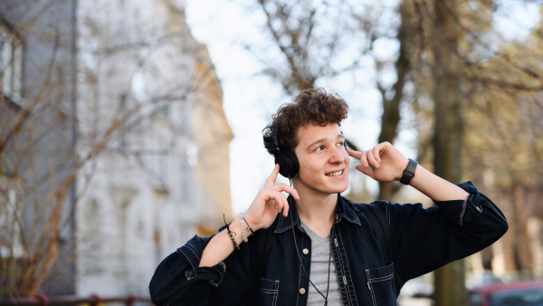 A portrait of young man commuter with headphones walking outdoors in city, listening to music.