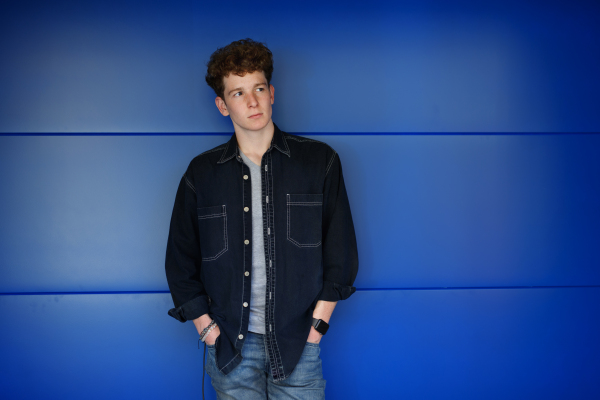 Front view portrait of young man standing against blue background outdoors.