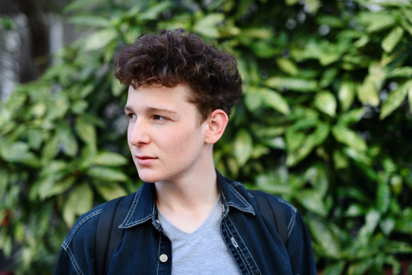 A close-up portrait of young man against green background outdoors.