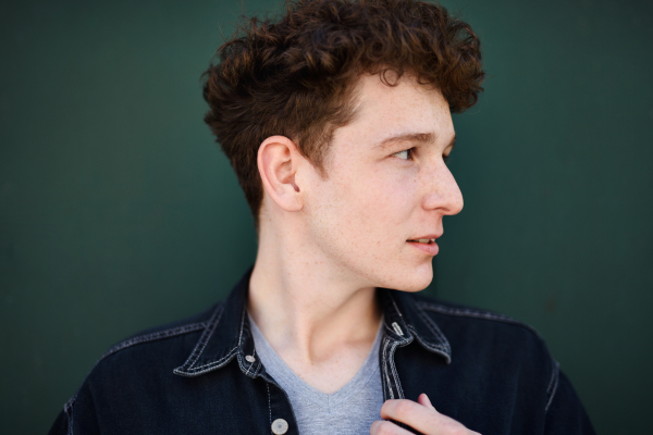 A close-up portrait of young man against green background outdoors.