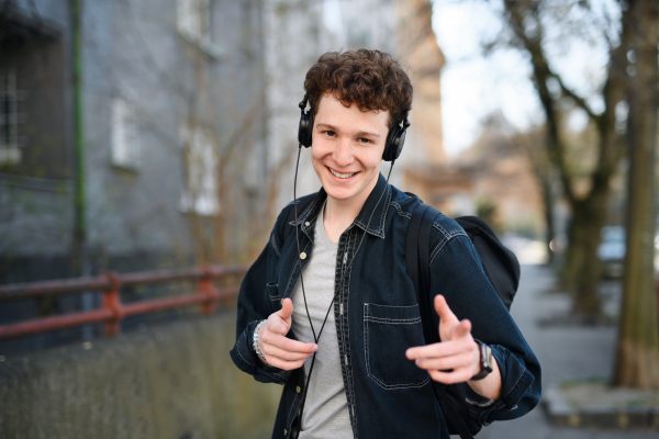 A portrait of young man commuter with headphones walking outdoors in city, looking at camera.