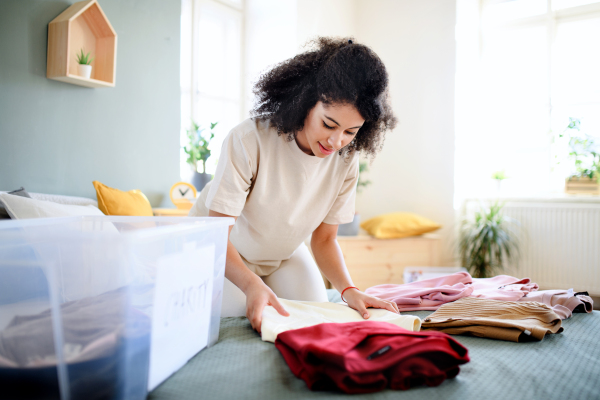 Happy young woman sorting wardrobe indoors at home, charity donation concept.