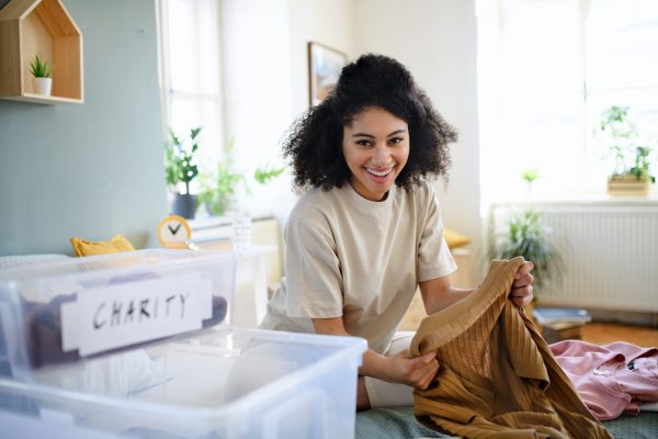 Happy young woman sorting wardrobe indoors at home, charity donation concept.