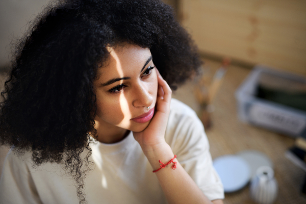 Close-up portrait of sad and tired young woman indoors, resting.