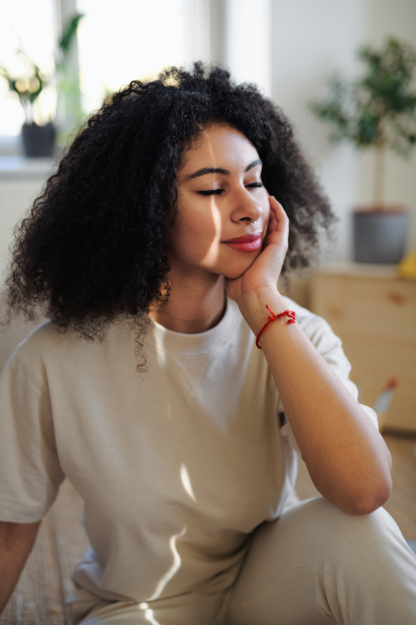 Portrait of contented young woman with closed eyes indoors, resting.