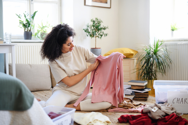 Happy young woman sorting wardrobe indoors at home, charity donation concept.