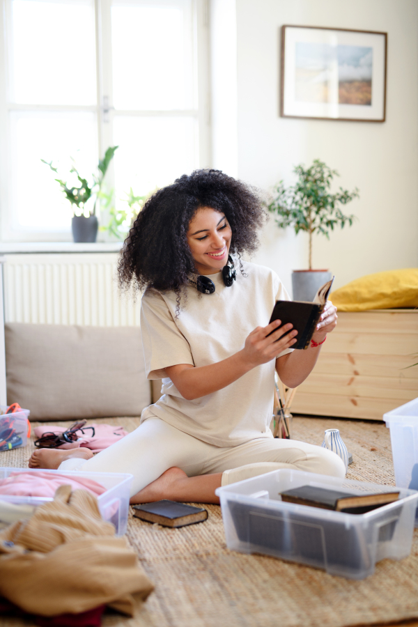 Happy young woman sorting clothes and books indoors at home, charity donation concept.