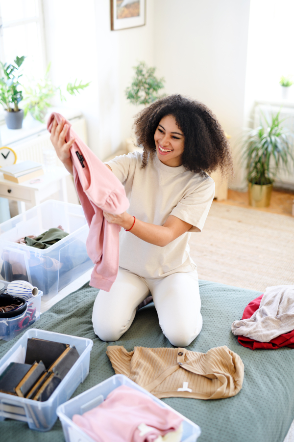 Happy young woman sorting wardrobe indoors at home, charity donation concept.