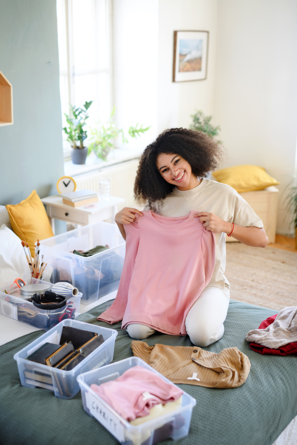 Happy young woman sorting wardrobe indoors at home, charity donation concept.