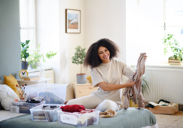 Happy young woman sorting clothing indoors at home, charity donation concept.