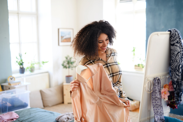 Happy young woman sorting wardrobe indoors at home, charity donation concept.