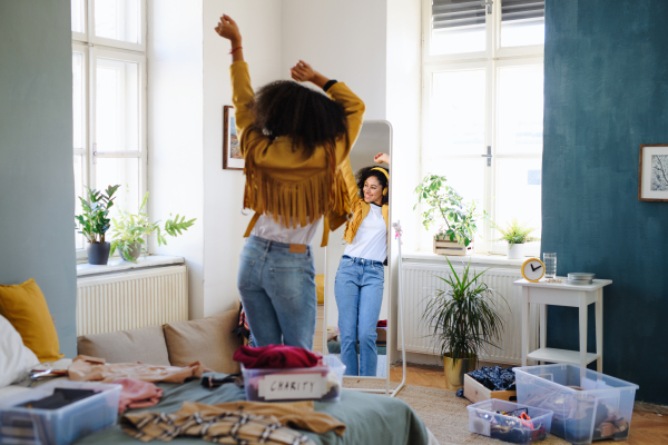 Rear view of cheerful young woman sorting wardrobe indoors at home, charity donation concept.