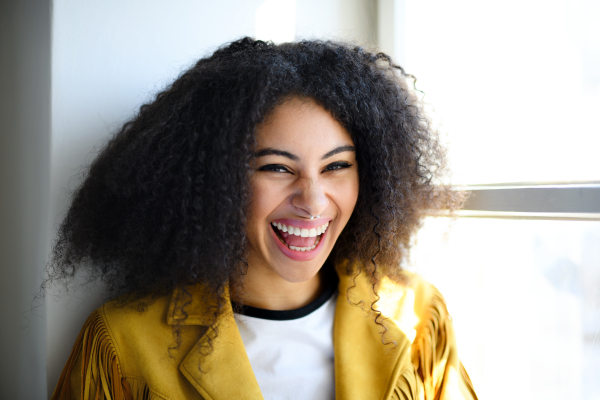 Close-up front view portrait of laughing young woman indoors, looking at camera.