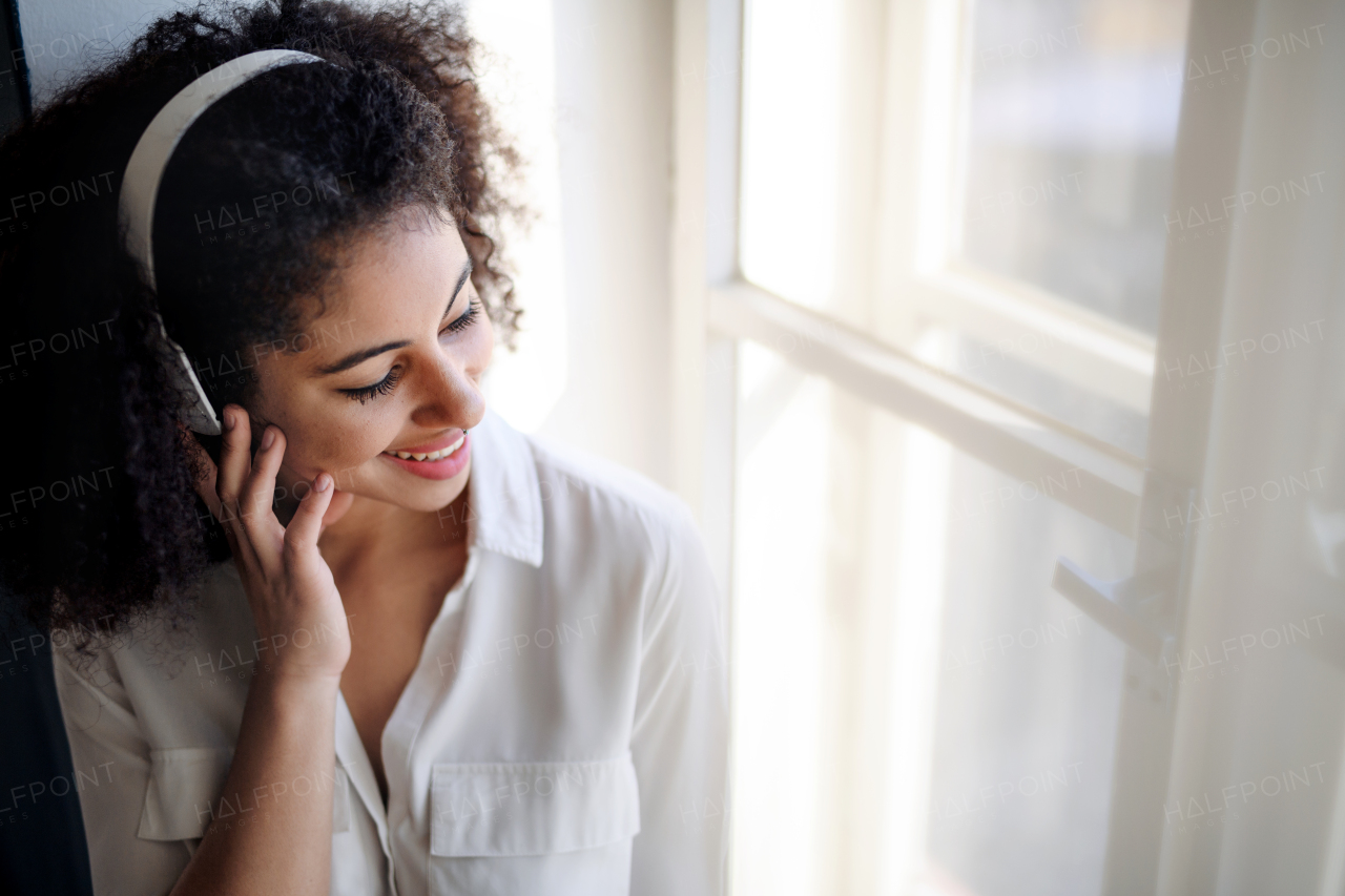 A portrait of young woman with headphones indoors at home, listening to music.