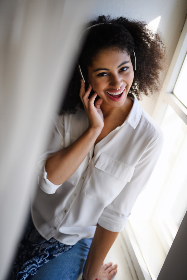 A portrait of young woman with headphones indoors at home, listening to music.