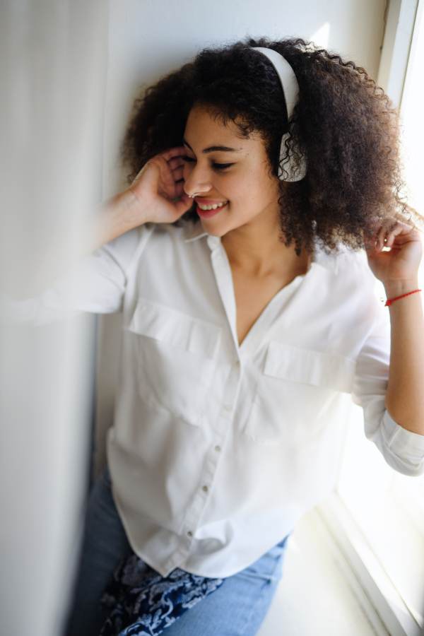 A portrait of young woman with headphones indoors at home, listening to music.