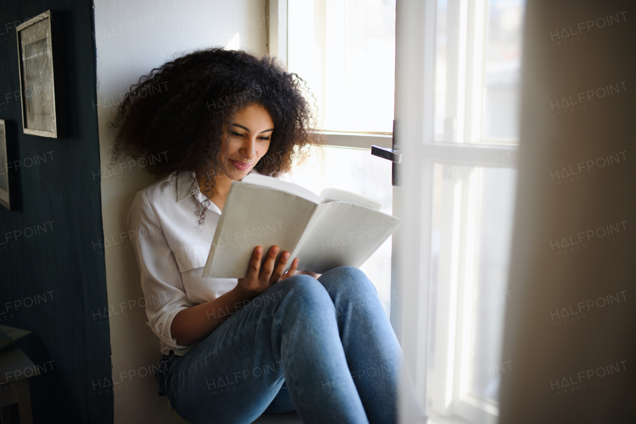 A portrait of young woman with book indoors at home, reading.