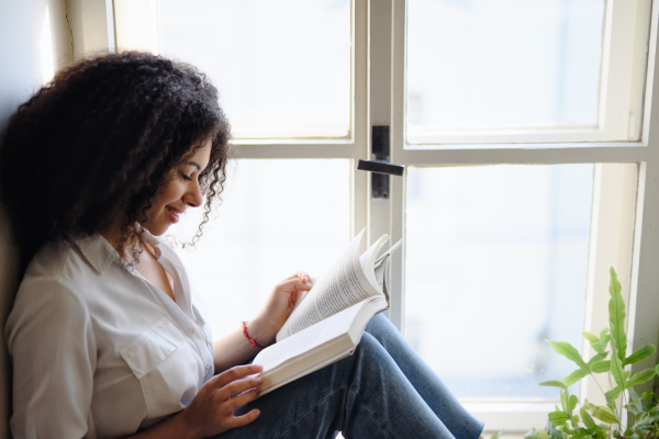 A portrait of young woman with book indoors at home, reading.