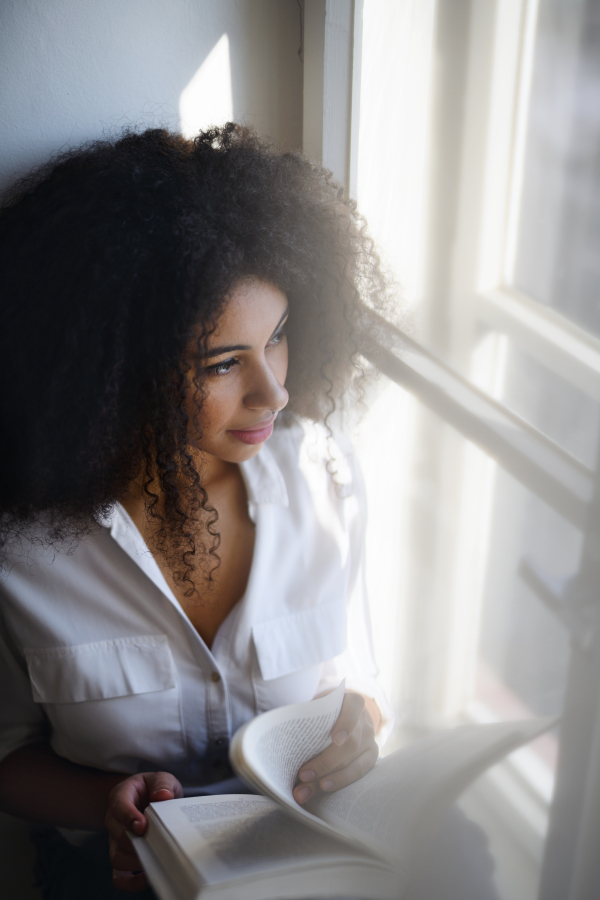 A portrait of young woman with book indoors at home, reading.