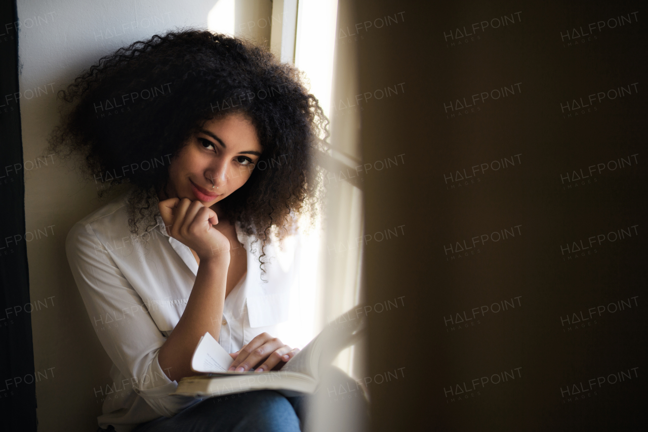 A portrait of young woman with book indoors at home, reading.