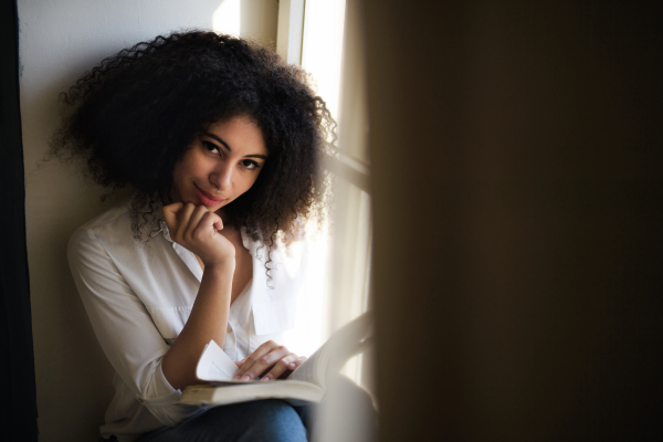 A portrait of young woman with book indoors at home, reading.