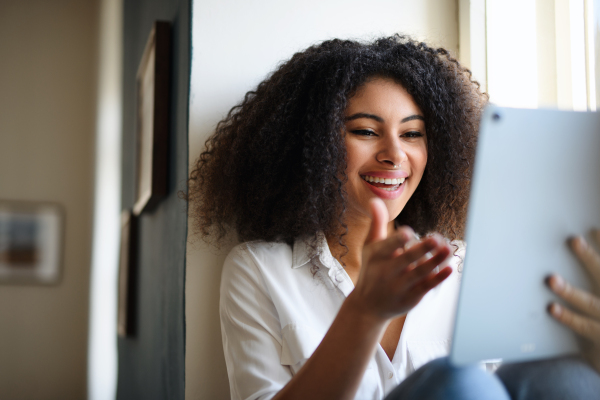 Portrait of young woman with tablet on window sill indoors at home, video call concept.