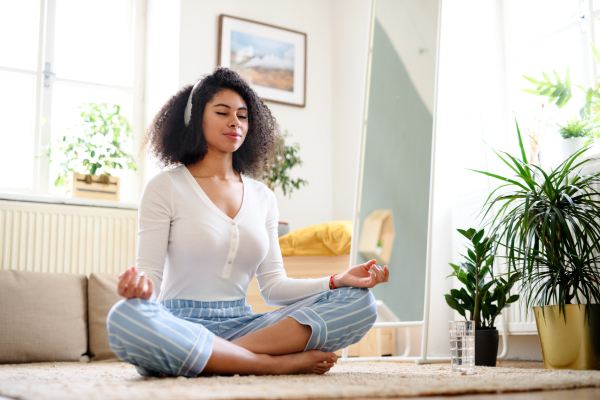 Portrait of relaxed young woman indoors at home, doing yoga exercise.