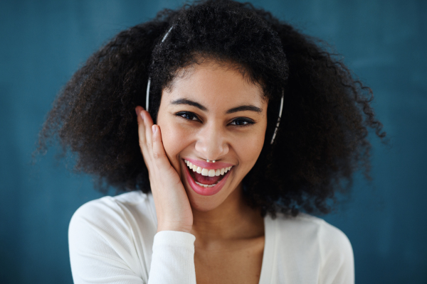 Close-up portrait of young woman with headphones indoors at home, listening to music.